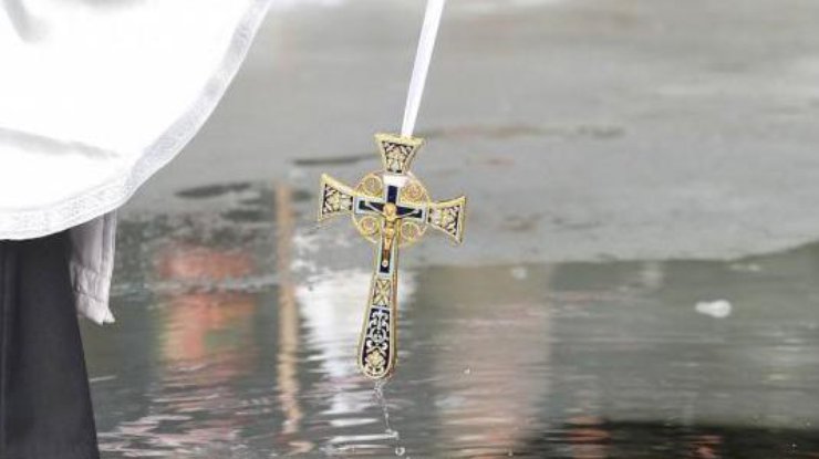 Священник опускает крест в воду/ фото: podrobnosti.ua